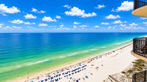 A beach with clear blue water, a sandy shore, and a balcony overlooking the ocean.