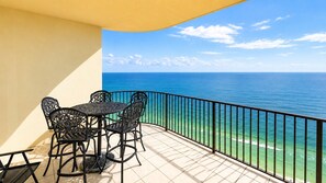 A balcony with a table and chairs, overlooking a clear blue sea.