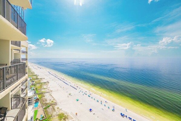 A beach with a clear view of the ocean, a pool, and a building with balconies.