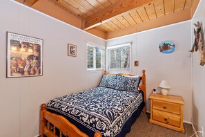 Une chambre avec un plafond en bois, un lit avec une literie à motifs, une table de chevet avec une lampe et un mur orné de tableaux encadrés.