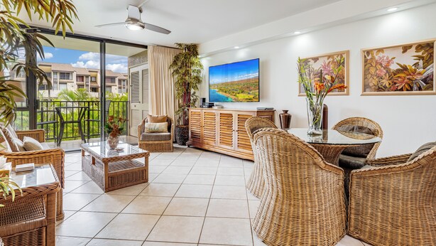 A spacious living area with wicker furniture, a large flat-screen TV, and a balcony with a view of buildings and greenery.