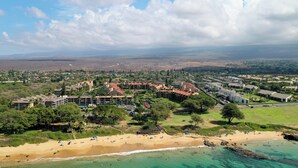 An aerial view of a coastal resort with multiple buildings, a sandy beach, and clear turquoise waters.