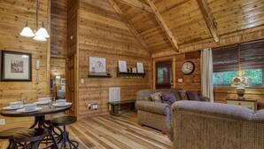 L’intérieur chaleureux d’un chalet, avec des murs et un plafond en bois, une table à manger avec des chaises, un canapé et une horloge au mur.