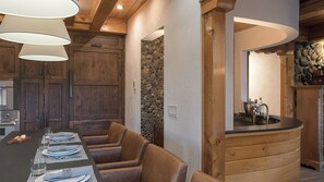 Interior de madera con una mesa de comedor para cuatro, una pared de piedra y una zona de cocina con un fregadero y utensilios.