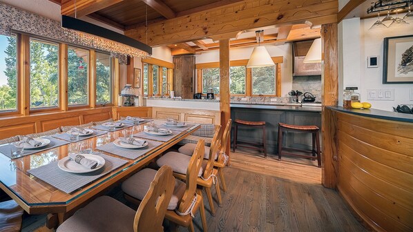Un intérieur en bois avec une table à manger pour six personnes, un coin cuisine et de grandes fenêtres.