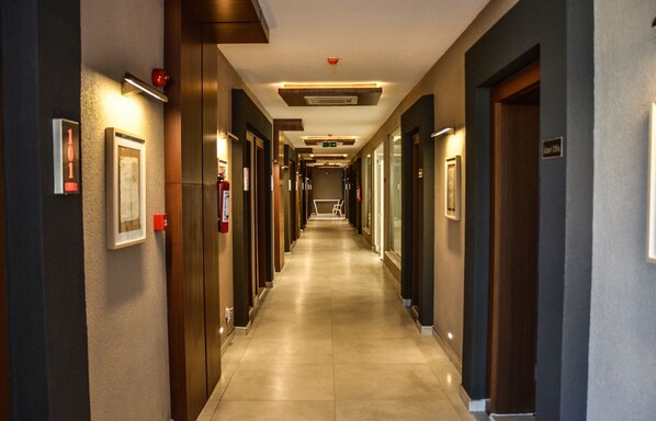 A hotel corridor with doors on both sides, a fire extinguisher, and a sign indicating the location of the elevator.