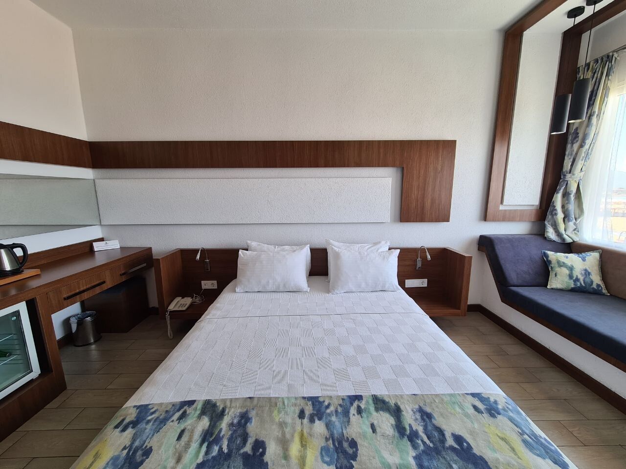 Habitación de hotel con una cama grande, un escritorio con teléfono, una mesita con tetera y un sofá con cojines.