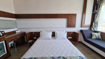 Habitación de hotel con una cama grande, un escritorio con teléfono, una mesita con tetera y un sofá con cojines.