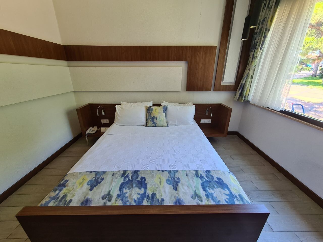 Una habitación de hotel con una cama grande, mesitas de noche, un teléfono y una ventana con cortinas.