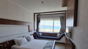 Une chambre d’hôtel comprenant un lit, un bureau, une fenêtre donnant sur la plage et un banc intégré.