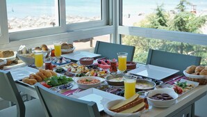 Une table de petit-déjeuner avec divers plats et boissons, donnant sur une plage et offrant une vue sur l’océan.