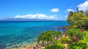 Una playa tropical con aguas turquesas cristalinas, costa rocosa y exuberante vegetación.