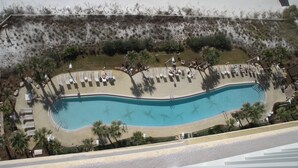 Vista aérea de un resort con piscina, tumbonas y palmeras.