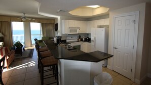 Una cocina moderna con una isla grande, armarios blancos y vista al océano.
