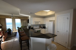 A modern kitchen with a large island, white cabinetry, and a view of the ocean.