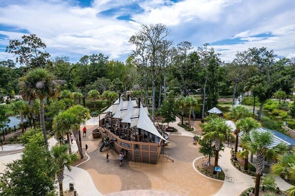 A large, open-air structure with a curved roof, surrounded by palm trees and other greenery.