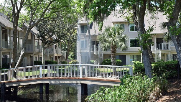 Zona residencial con un puente sobre un cuerpo de agua, rodeada de árboles y edificios de varios pisos con balcones.