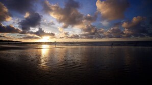 A beach with a sunset, calm water, and a few people walking. - All About Location! Perfect, Well Equipped Condo 300 Yards From Beach, 2 Pools (Tamarindo)