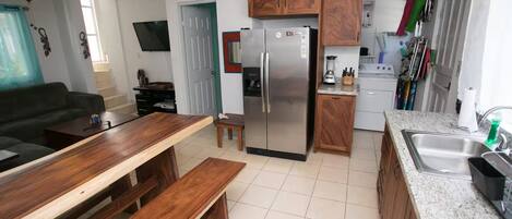A compact kitchen with a refrigerator, wooden cabinets, a countertop, and a dining area with a bench.