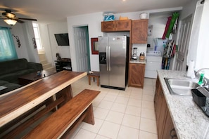 A compact kitchen with a refrigerator, wooden cabinets, a countertop, and a dining area with a bench. - All About Location! Perfect, Well Equipped Condo 300 Yards From Beach, 2 Pools (Tamarindo)