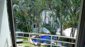 A balcony with wicker furniture, a tiled floor, and a view of a swimming pool and palm trees. - All About Location! Perfect, Well Equipped Condo 300 Yards From Beach, 2 Pools (Tamarindo)