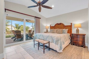Une chambre avec un grand lit, un ventilateur de plafond, une table de chevet et une vue sur un balcon équipé de chaises.
