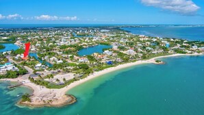 An aerial view of a coastal resort area with a beach, clear blue waters, and a dense cluster of buildings.