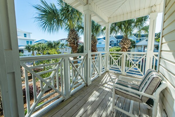 A covered porch with a bench, white railings, and palm trees.
