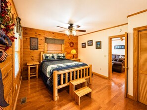A wooden-floored bedroom with a bed, a ceiling fan, and a small wooden bench.