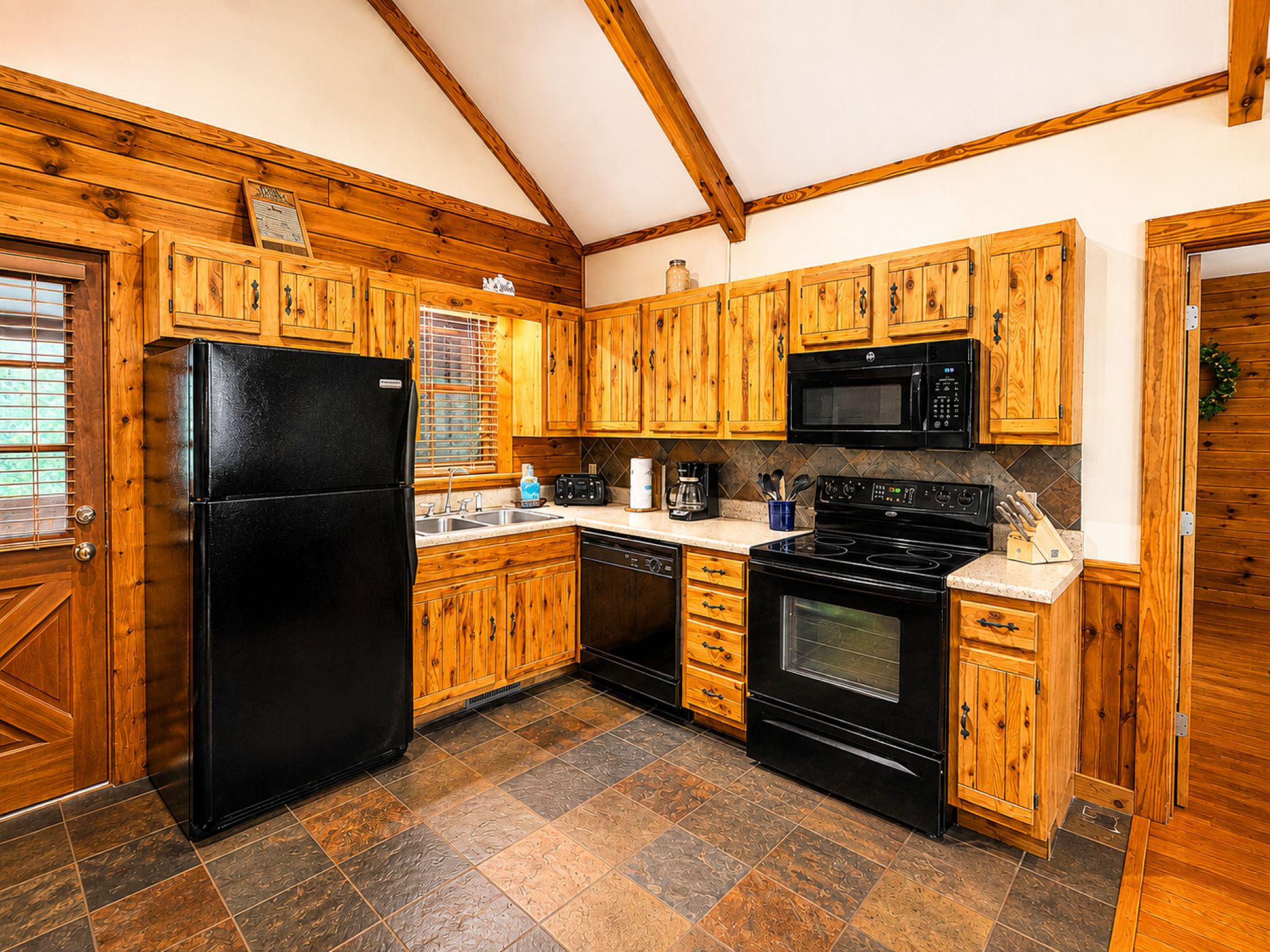 Une cuisine avec des meubles de rangement en bois, un réfrigérateur noir, un four à micro-ondes, une cuisinière et un lave-vaisselle.