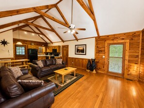 A spacious living room with a high ceiling, wooden beams, a ceiling fan, a fireplace, and a dining area with wooden furniture. - ER79 - Robyn's Nest - Great location. Close to all the action! (Pigeon Forge)