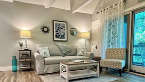 Una sala de estar con un sofá, un sillón estampado, una mesita de centro y una estantería.