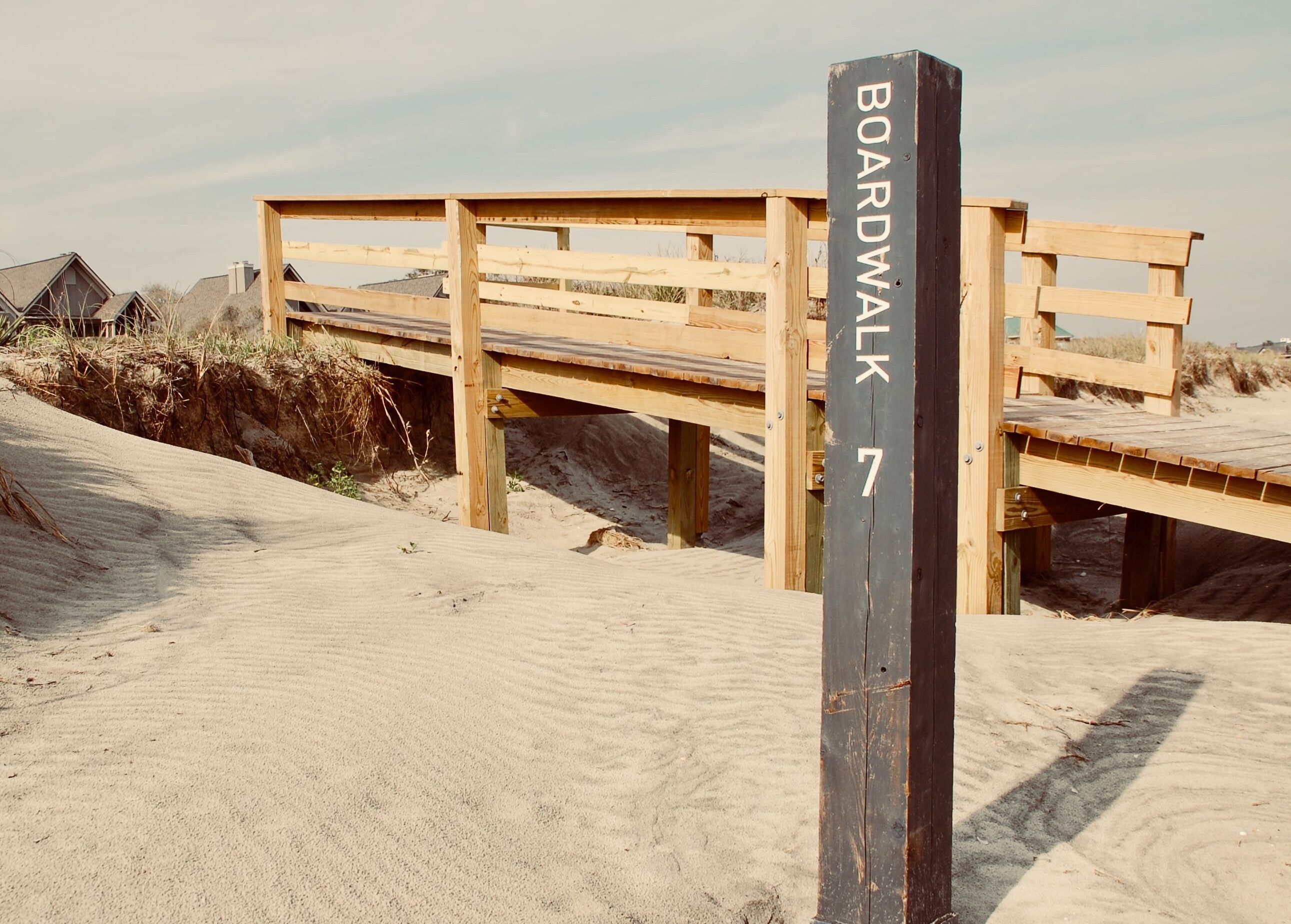 A wooden boardwalk labeled 'BOARDWALK 7' in a sandy area with wooden structures in the background.