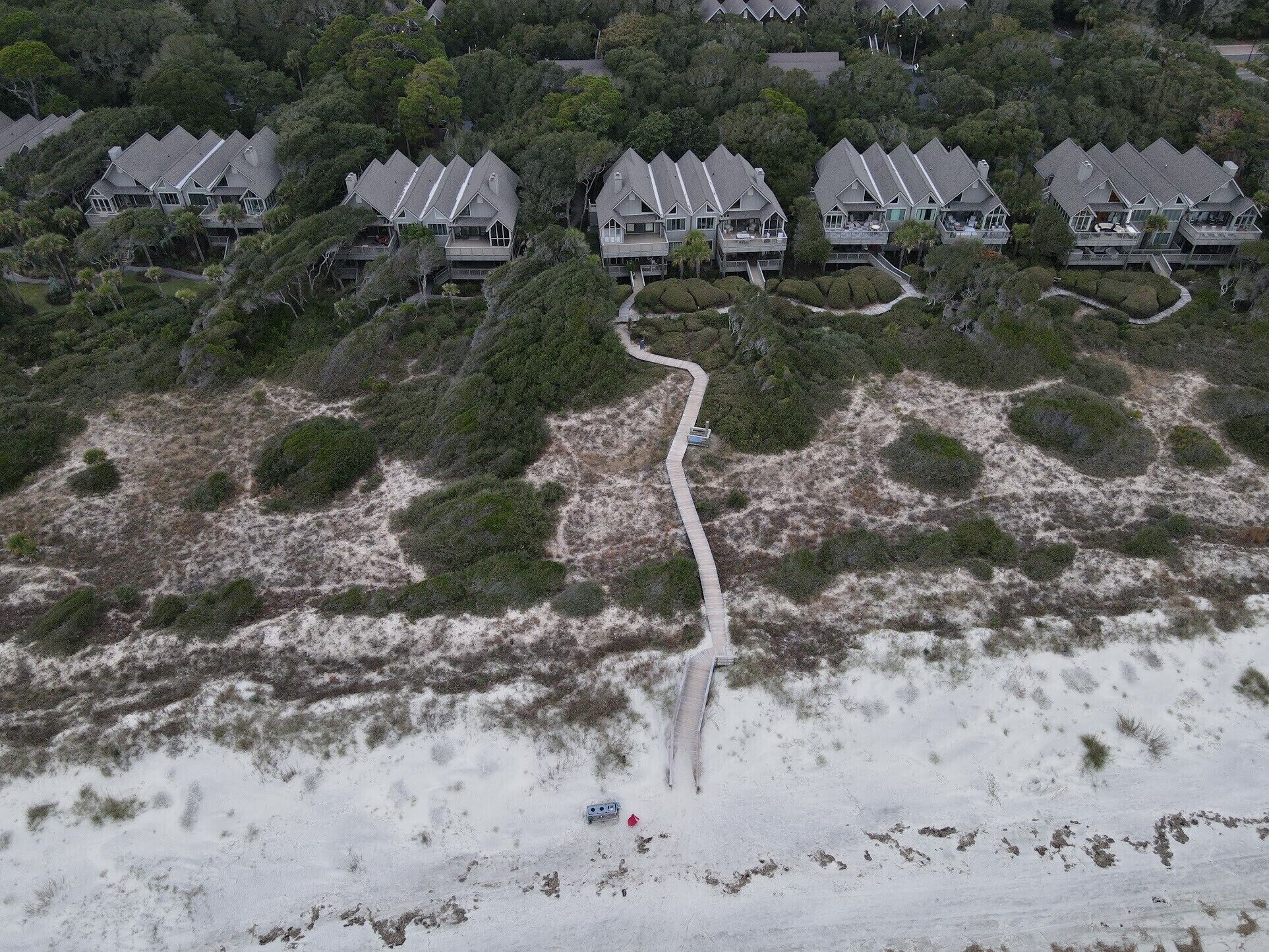 Vista aérea de una zona residencial costera con varias casas, una playa de arena y un camino sinuoso.