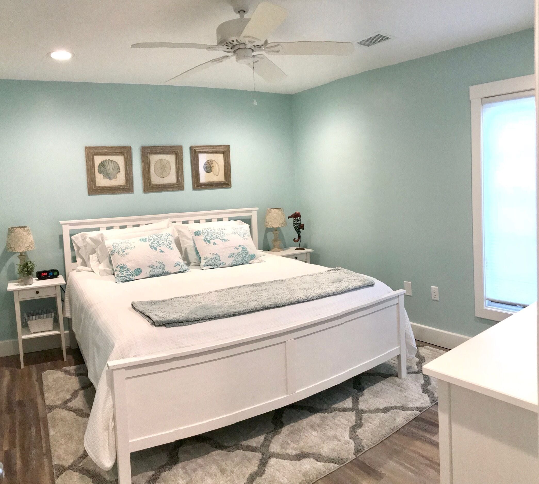 Quarto com cama branca, ventilador de teto e mesa de cabeceira com abajur.