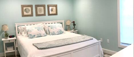 Quarto com cama branca, ventilador de teto e mesa de cabeceira com abajur.