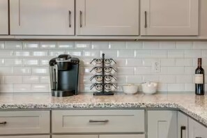 Una cocina moderna con armarios blancos, una cafetera, una botella de vino y un esclavo de especias.