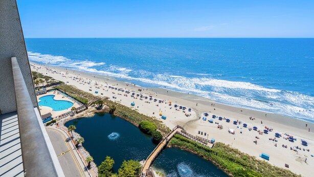 A beach with a pool, umbrellas, and a bridge.