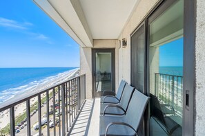 Un balcon avec vue sur la plage et l’océan, une porte et deux chaises.
