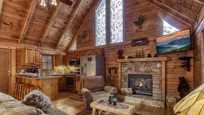 Een gezellig interieur van een chalet met een stenen openhaard, houten wanden, een keukenhoek en een comfortabele zithoek.