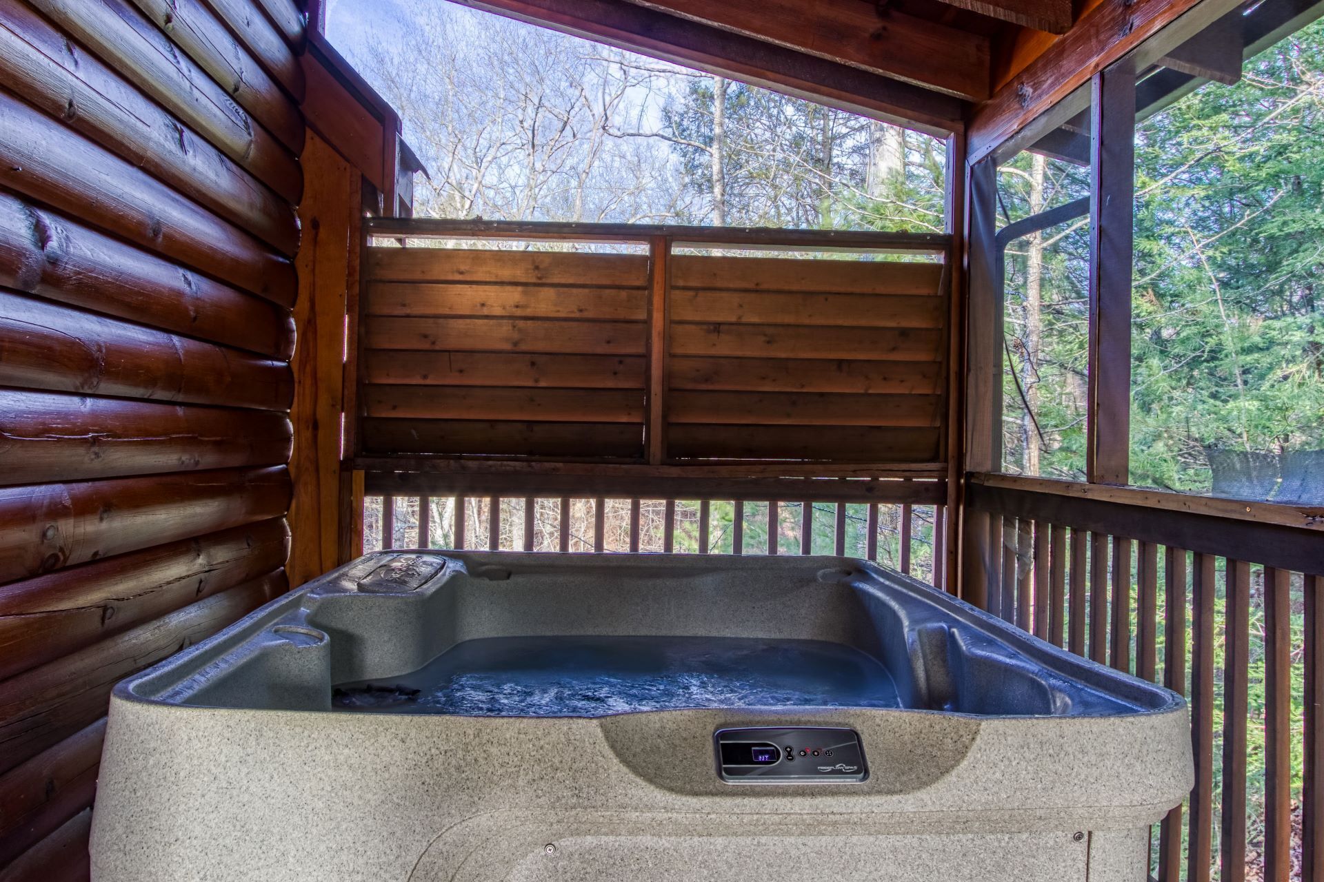 Un bain à remous dans un chalet en bois, doté d’une terrasse en bois et offrant une vue sur les arbres.