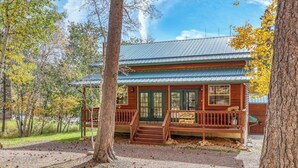 Eine rustikale Holzhütte mit Veranda, umgeben von Bäumen und einem Kiesweg.