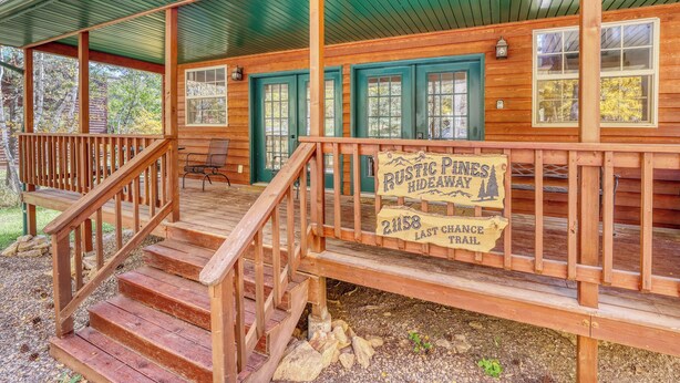 Eine rustikale Holzhütte mit Veranda, Holzstufen und einem Schild, das den Namen Rustic Pines Hideaway und den Lay Chase Trail anzeigt.
