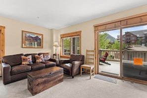 Un salon comprenant un ensemble de canapés, une table basse en bois, une lampe et une vue sur une montagne, visible à travers une grande porte-fenêtre coulissante.