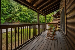A wooden deck with a rocking chair, surrounded by a wooden railing, overlooking a forested area. - Cozy 1BR cabin in Pigeon Forge with hot tub, fireplace, arcade, pool access. (Pigeon Forge)