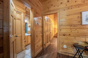 A wooden interior with a hallway leading to a bathroom and a small table with a chair.