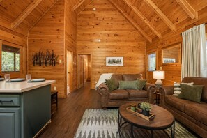A cozy cabin interior with a wooden ceiling, a living room with a brown leather sofa, a coffee table, and a kitchen area with a counter and cabinets. - Cozy 1BR cabin in Pigeon Forge with hot tub, fireplace, arcade, pool access. (Pigeon Forge)
