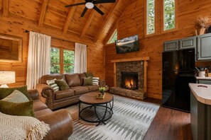 A cozy cabin interior with a stone fireplace, a leather sofa, a dining table, and a kitchen area. - Cozy 1BR cabin in Pigeon Forge with hot tub, fireplace, arcade, pool access. (Pigeon Forge)