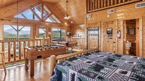 Eine Holzhütte mit einem Kicker, einem Bett mit einer Patchworkdecke und einem Balkon mit Bergblick.