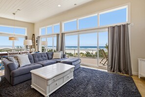 A spacious living room with a large sectional sofa, a white coffee table, and a view of the ocean through large windows.